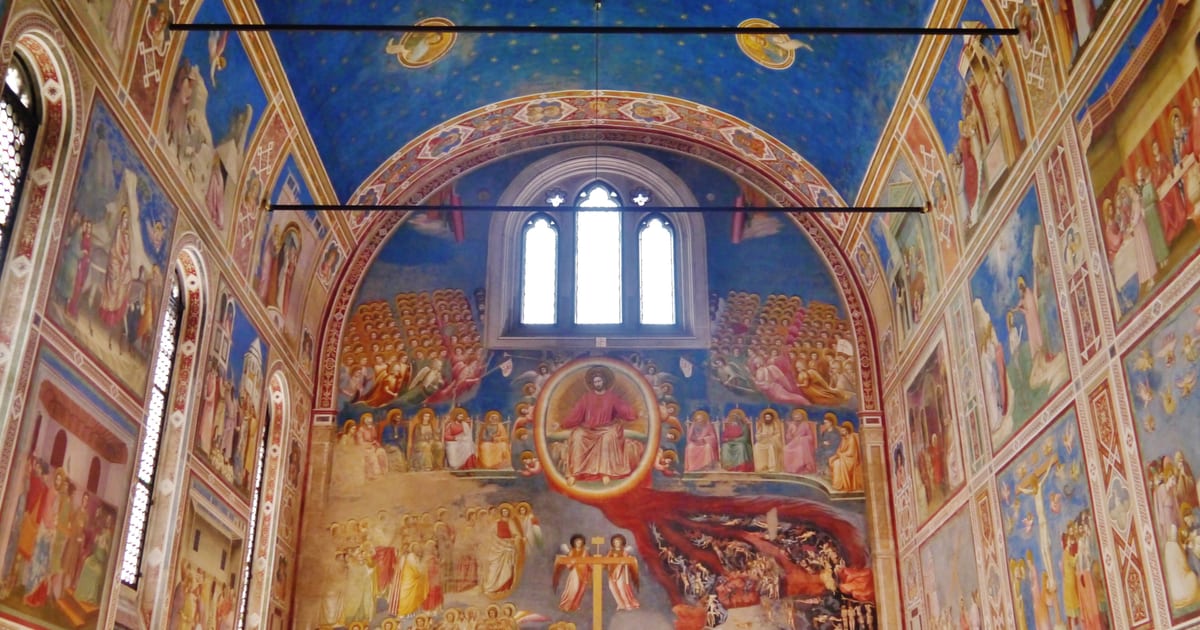 Inside the Scrovegni Chapel in Padua, looking towards Giotto's Last Judgement on the entrance wall beneath a blue vault scattered with gold stars, with fresco panels covering the side walls
